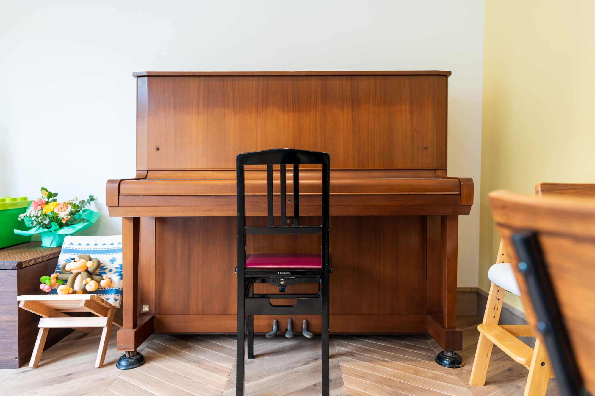 木目のアップライトピアノとマゼンタ色の座面の椅子。花束や小さな椅子も見える明るいラウンジ